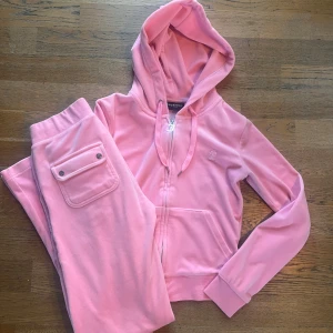 Rosa velourset från Juicy Couture XS - Säljer ett snyggt rosa velourset från Juicy Couture med hoodie och byxor. Hoodien har dragkedja och byxorna har en praktisk ficka med knapp. Använd en gång, som nytt!