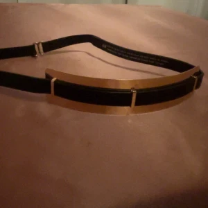 Svart och guld bälte från H&M - Snyggt bälte från H&M i svart med gulddetaljer. Perfekt för att ge en elegant touch till din outfit. Justerbar storlek för bästa passform.