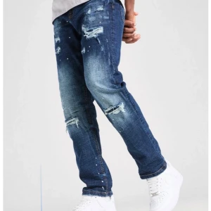 Blå distressed jeans - Snygga blå jeans med en cool distressed look från Sophia & Gerard. De har en straight passform och är dekorerade med slitningar och små färgstänk för en trendig stil. Perfekta för en avslappnad look.