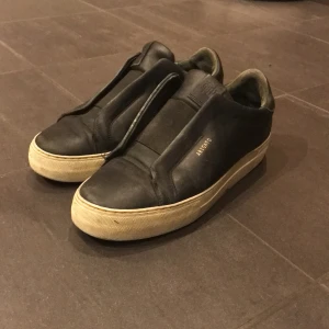 Svarta sneakers från Axel Arigato - Snygga svarta sneakers från Axel Arigato med en stilren design. Skorna har en vit sula och är tillverkade i skinn. Perfekta för en avslappnad och trendig look.