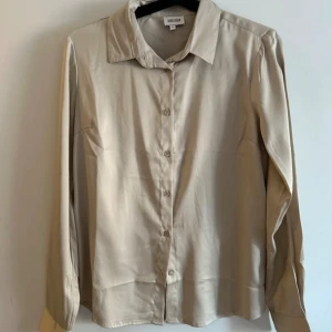 Beige skjorta från Bubbleroom - Snygg beige skjorta från Bubbleroom i storlek 34. Skjortan har långa ärmar och knappar framtill. Perfekt för en stilren look. I mycket gott skick, endast använd ett fåtal gånger