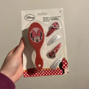 Hårborste och hårklämmor med Minnie Mouse från Disney - Säljer ett set med en röd hårborste och matchande hårklämmor med Minnie Mouse-motiv. Perfekt för barn som älskar Disney och vill ha en rolig håraccessoar. Setet innehåller en borste och två klämmor, alla dekorerade med den ikoniska Minnie Mouse-rosetten.