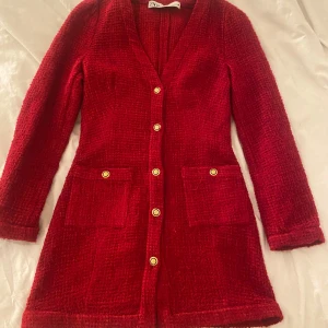 Röd klänning från Zara - Snygg röd klänning från Zara med guldknappar och två fickor framtill. Den har en v-ringad design och långa ärmar, perfekt för att ge en elegant touch till din outfit.