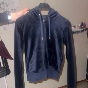 Mörkblå velour hoodie från Juicy Couture - Säljer en snygg mörkblå velour hoodie från Juicy Couture. Den har dragkedja framtill och en broderad logga på bröstet. Perfekt för en avslappnad och stilren look.