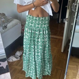 Grön och vit mönstrad långkjol - Snygg långkjol i grönt och vitt med ett unikt mönster. Kjolen har en elastisk midja för bekväm passform och ett luftigt fall som passar perfekt för varma dagar. Skriv till mig gällande mer frågor!💕