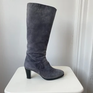 Grå stövlar från Juhani Palmroth - Eleganta grå stövlar i mocka från Juhani Palmroth med en dekorativ detalj på sidan. Stövlarna har en dragkedja för enkel på- och avtagning samt en bekväm klack.