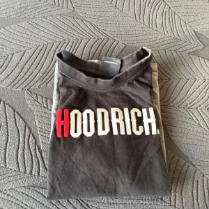 Svart och grå t-shirt från Hoodrich - Snygg t-shirt från Hoodrich i svart och grått med röd detalj på ärmarna. Stort tryck med märkesnamnet på bröstet. Perfekt för en casual look.