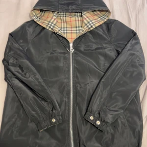 Burberry reversible jacka - Snygg svart jacka från Burberry med klassiskt rutigt foder. Jackan har en dragkedja framtill och en huva. Perfekt för en stilren look.