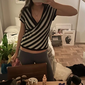 Randig omlottopp i svart och silver - Snygg omlottopp med korta ärmar i svart och silver. Toppen har ett randigt mönster och en v-ringad design som ger en stilren look. Perfekt för en kväll ute eller en festlig tillställning.