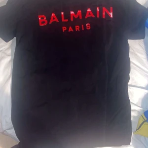 Svart t-shirt från Balmain - Snygg svart t-shirt från Balmain med röd text på bröstet. Perfekt för en stilren look.                                Skriv gärna vid intresse och äkta såklart från Dubai:)