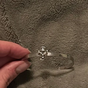 Silverfärgat armband med dödskalle - Snyggt och stilrent armband i silverfärg med en cool dödskalle som detalj. Perfekt för att ge din outfit en edgy touch. Armbandet är öppet och justerbart för att passa de flesta handleder.