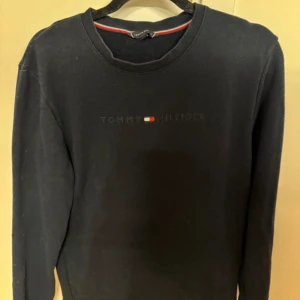 Svart tröja från Tommy Hilfiger - Snygg svart tröja från Tommy Hilfiger med långärmad design. Tröjan har en diskret logga på bröstet och är perfekt för en stilren look. Passar bra till både jeans och chinos.