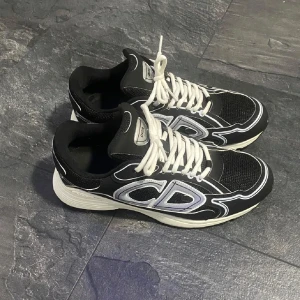 Dior b30 - Snygga svarta sneakers med vita snören och detaljer. Skorna har en sportig design med en bekväm sula och tydliga CD-loggor på sidorna. Perfekta för en stilren look . Säljer för 2500