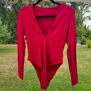 Röd body - En röd body i stretchigt skön material ❣️ Tre knappar längst ner och v-ringad. Storleken är M och den är lite för stor för mig, därför säljer jag den nu!  (ALDRIG ANVÄND)  Längd: 75 cm Axel: 34 cm Byst: 82 cm Midja: 70 cm