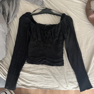 Svart långärmad topp - Säljer en elegant svart topp med långa ärmar. Den har en snygg rynkad design som ger en fin struktur och en v-ringad hals. Perfekt för både vardag och fest!
