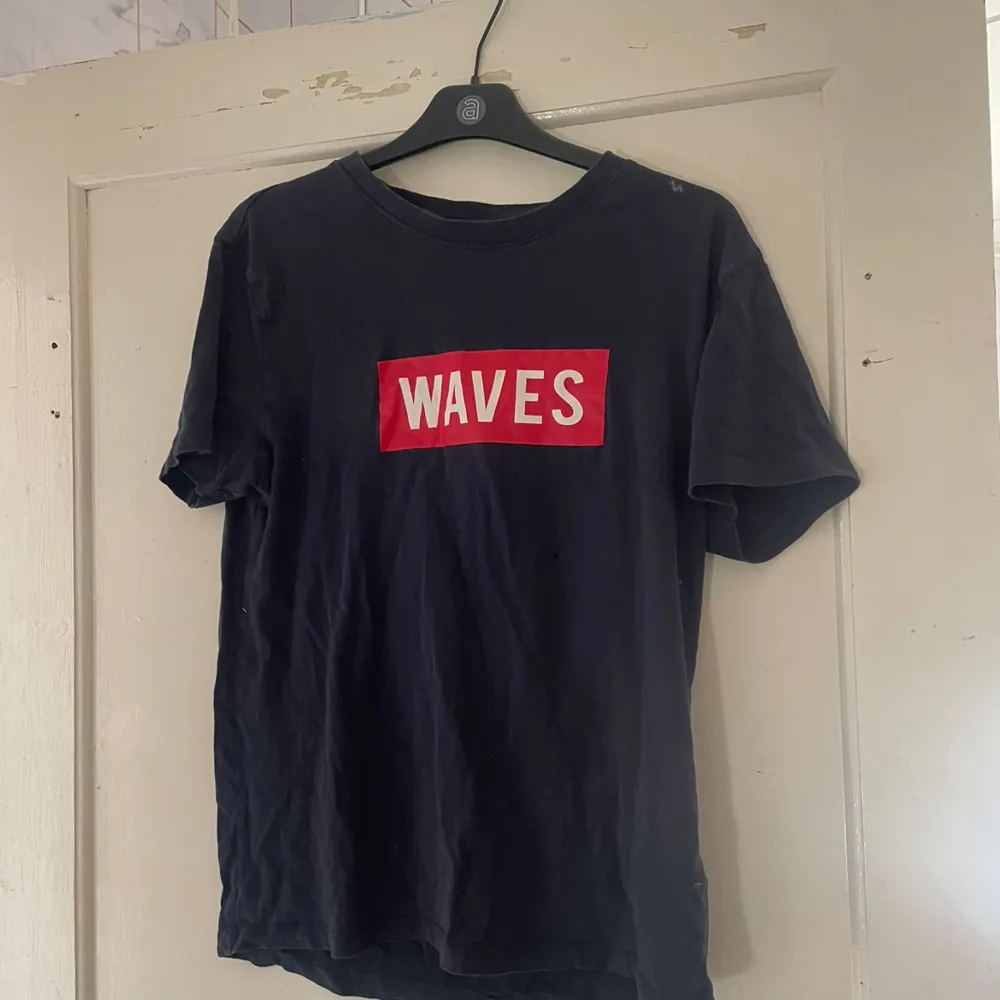 Säljer en svart t-shirt från 157 i storlek S. Den är gjord av 100% bomull och har ett coolt rött och vitt 'WAVES' tryck på framsidan. Perfekt för en avslappnad stil!. T-shirts.