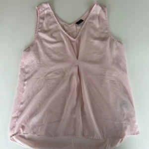 Ljusrosa ärmlös topp - Säljer ett rosa linne med insydd detalj på bröstet. Toppen är knappt använd och behöver hitta ett hem där den kommer till användning.