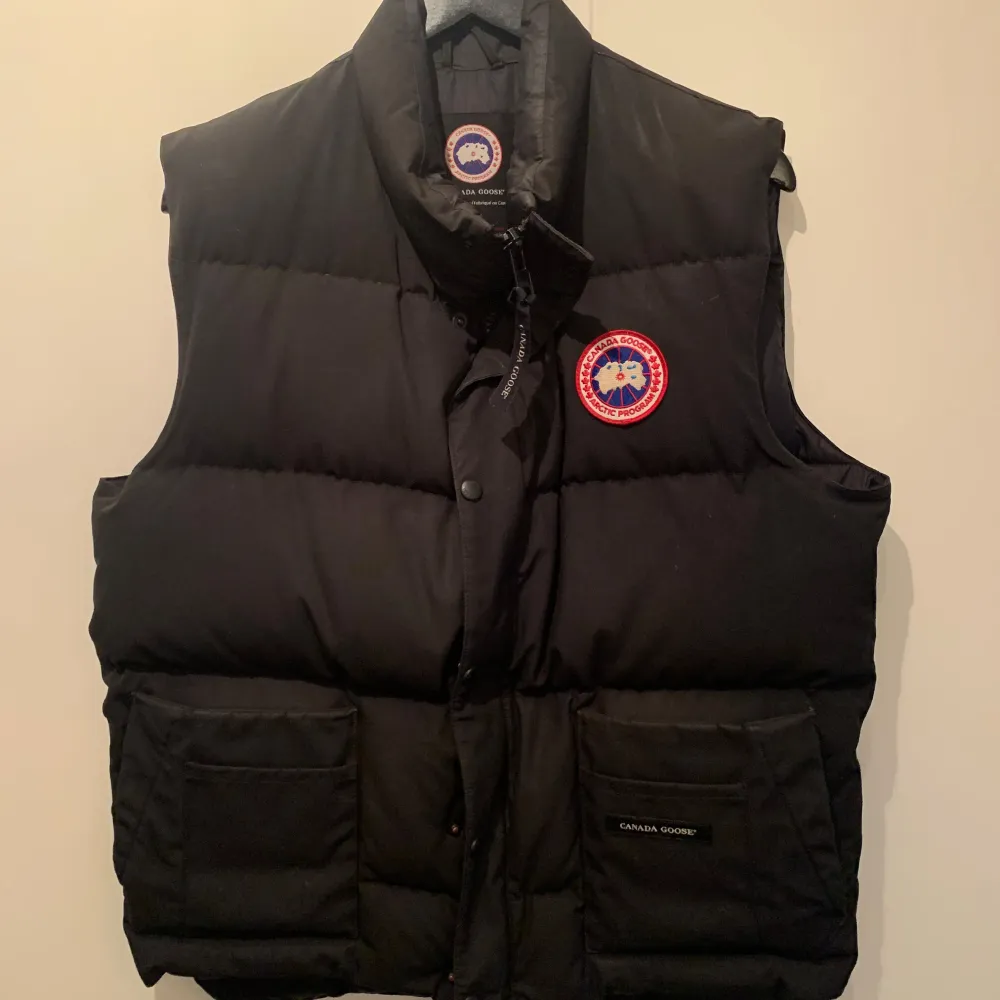 100% äkta Canada Goose väst i storlek M. Finns bevis på bilderna. Den är i färgen svart och i ett mycket bra skick förutom att sömmen på ena fickan framtill har släppt, men är enkel att fixa. . Jackor.