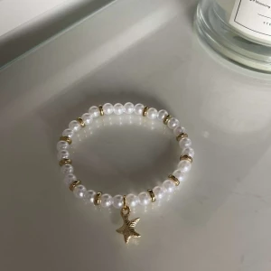 Pärlarmband med guldstjärna - Säljer ett superfint armband med vita pärlor och små gulddetaljer. Armbandet har en gullig guldstjärna som hänge, vilket ger det en extra touch av elegans. Perfekt för både vardag och fest!