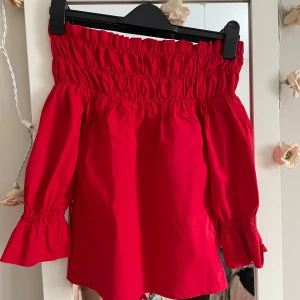Röd offshoulder topp från Pimkie - Snygg röd offshoulder topp från Pimkie med elastisk smockdetalj vid hals och ärmslut. Perfekt för en trendig look med volangdetaljer som ger extra stil. Passar bra till både jeans och kjol..storlek xs 