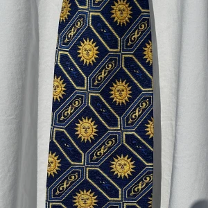 Vintage Gianni Versace Silkeslips - ✨ Versace silkeslips – sällsynt och ikonisk ✨  Säljer denna exklusiva Versace-slips i 100% silke, med ett unikt solmönster i guld och marinblått. En klassisk lyxdesign som ger en elegant touch till varje outfit.  🔹 Märke: Gianni Versace 🔹 Material: 100% silke 🔹 Färg: Blå och guld 🔹 Skick: Utmärkt skick – inga fläckar eller liknande 🔹 Sällsynt modell – går inte att hitta någon annanstans online!  Perfekt för både formella tillfällen och som ett statement-piece. Tveka inte att skriva om du har någ