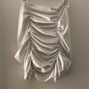 Vit draperad kjol från Shein - Snygg vit kjol från Shein med draperad design och dragkedja i sidan. Perfekt för att skapa en stilren look. Kjolen har en kort längd och är tillverkad i ett glansigt material som ger en lyxig känsla.