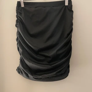 Svart kjol med rynkade detaljer - Snygg svart kjol med rynkade detaljer på sidorna. Tillverkad i polyester och spandex för en bekväm passform. Perfekt för att ge en stilren look.