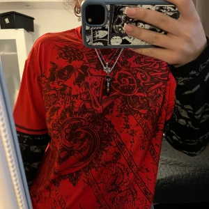 Röd och svart mönstrad t-shirt - Säljer en cool röd t-shirt med svart mönster. Den har en unik design med detaljerade tryck och långa ärmar i lager-på-lager-stil. Perfekt för en edgy look!