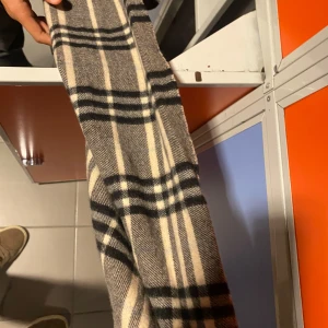 Rutig halsduk från Burberry - Snygg och klassisk rutig halsduk från Burberry i beige, svart och grått. Perfekt för att hålla dig varm och stilren under kyliga dagar. Denna halsduk är ett måste för alla modeintresserade!