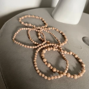 Beige armband med facetterade pärlor - Snyggt beige armband med små facetterade pärlor som ger en glittrig effekt. Perfekt för att lägga till en subtil touch av elegans till din outfit. Armbandet är elastiskt och passar de flesta handleder. Aldrig använda