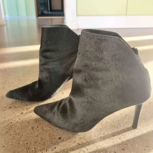 Svarta boots med spetsig tå strl 39  - Snygga svarta boots med spetsig tå och klack. Tillverkade i ett material som liknar päls vilket ger en lyxig känsla. Perfekta för att höja din stil till nästa nivå.