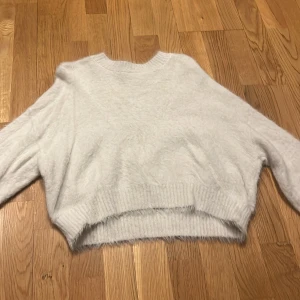 Vit fluffig tröja från H&M - Mysig vit fluffig tröja från H&M. Perfekt för kyliga dagar med sin mjuka och varma känsla. Tröjan har en rund halsringning och ribbade kanter som ger en stilren look.