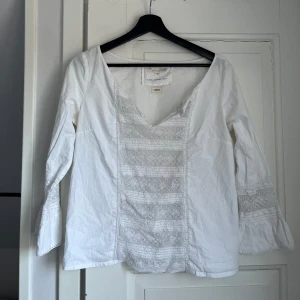 Vit blus med spetsdetaljer - Säljer en vit blus från Sample med vackra spetsdetaljer framtill och på ärmarna. Blusen har en v-ringad design och långa ärmar. Perfekt för en stilren och elegant look. storlek S