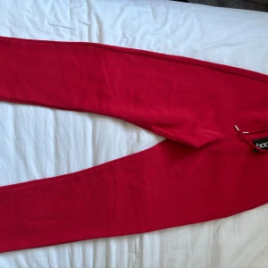Röda mjukisbyxor från Boohoo - Snygga röda mjukisbyxor från Boohoo med elastisk midja. Perfekta för en avslappnad stil. Byxorna har en loose passform och är tillverkade i mjukt material för extra komfort. Passar både Xs/S. 