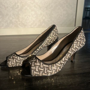 Mönstrade pumps med öppen tå - Snygga kitten heels / pumps med mönster i svart och guld, öppen tå. Lägre klack och bra skick! På insidan börjar dock tyget lossa, se bild 5. Köpta på vinted men passade ej mig ❤️Svensk storlek står ej men motsvarar 38, (har vanligtvis 37)
