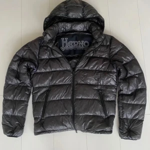 Svart/grå pufferjacka från Herno - Snygg svart jacka från Herno med dragkedja och huva. Jackan har en quiltad design och är perfekt för kyligare dagar. Säljer den pga att den inte passar, den är i ny med inga defekter men inget annat än jackan ingår, Passar M/S, skick 10/10 och jag är öppen för byten också