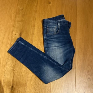 Blå jeans från Replay med riktigt skön tvätt - Snygga vintage blå jeans från Replay med en klassisk femficksdesign och lätt slitna detaljer. De har en dragkedja och knapp framtill. Byxorna har en riktigt skön tvätt. Liten fläck på ena benet.