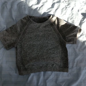 Grå kortärmad tränings topp - Säljer en stilren grå kortärmad tröja med ett melerat mönster. Perfekt för en avslappnad look. Tröjan har en rund halsringning och är tillverkad i ett mjukt material. Denna är till träning och är som en topp🩶🥊