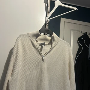Vit ribbad tröja från H&M - Säljer en stilren vit ribbad tröja från H&M med dragkedja vid halsen. Perfekt för en avslappnad och trendig look. Tröjan har en slim fit passform och långa ärmar.