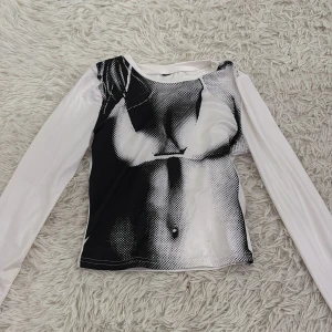 Svartvit långärmad topp med tryck - Snygg svartvit långärmad topp med ett unikt tryck som ger en cool effekt. Perfekt för att sticka ut i mängden. Tillverkad i ett mjukt och stretchigt material för en bekväm passform.