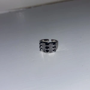 Silverfärgad ring med hjärtdetaljer - Snygg och trendig silverfärgad ring med små hjärtan och glittriga detaljer. Perfekt för att ge en edgy touch till din stil. Ringen är justerbar och passar de flesta storlekar.