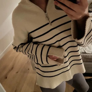 Beige och svart randig tröja med dragkedja - Säljer en mysig beige tröja med svarta ränder och dragkedja vid halsen. Tröjan har långa ärmar och ribbade muddar. Perfekt för en avslappnad stil.