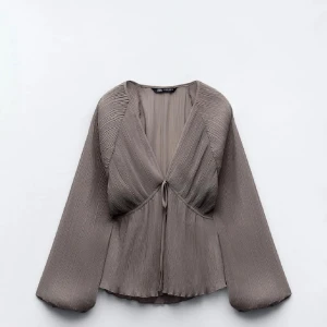 Plisserad blus från Zara - Grå blus från Zara med plisserade detaljer och knytning framtill. Blusen har långa vida ärmar och en v-ringad design som gör blusen fin till både fest och vardag!😍