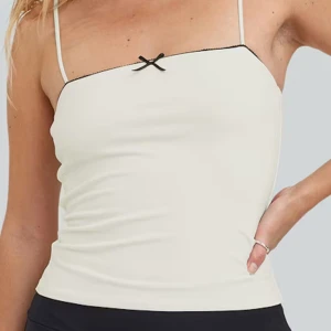 Vit topp med svart rosett - Jätte fin vit topp med smala axelband och en söt svart rosett framtill. Köpt på Bikbok men aldrig använd. 