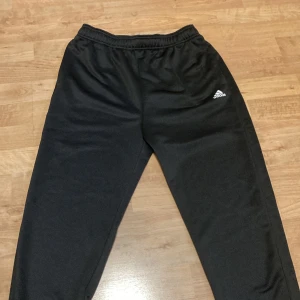 Svarta mjukisbyxor från Adidas - Säljer ett par svarta mjukisbyxor från Adidas. Byxorna har en elastisk midja och är perfekta för en avslappnad stil. Adidas-loggan är tryckt på ena benet.