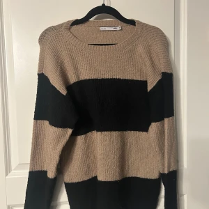 Beige och svart randig stickad tröja  - Säljer en mysig stickad tröja från Lager 157 i beige och svart med breda ränder. Tröjan har en rund halsringning och långa ärmar, perfekt för kyligare dagar. Den är i storlek 150 och passar bra för en avslappnad stil.