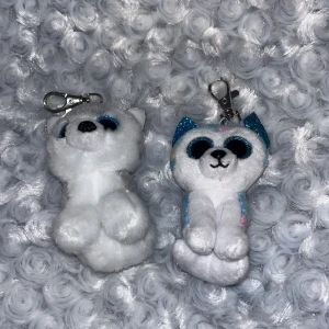Två söta nyckelringsdjur  - Två små plyschdjur med nyckelringar. Ena är en vit och grå hund med blå glittriga ögon. Den andra är en vit och blå hund med färgglada prickar och blå glittriga ögon.💘Perfekta som accessoarer för väskan eller nycklarna. Nypris 50kr/st💕