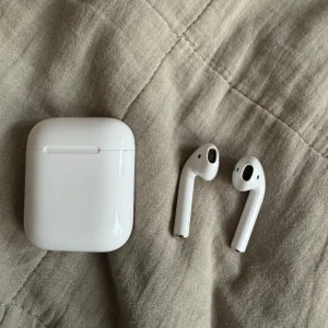 Trådlösa hörlurar med laddningsetui - Säljer ett par vita trådlösa hörlurar med tillhörande laddningsetui. Perfekta för musik och samtal på språng. Smidig och kompakt design som enkelt får plats i fickan.