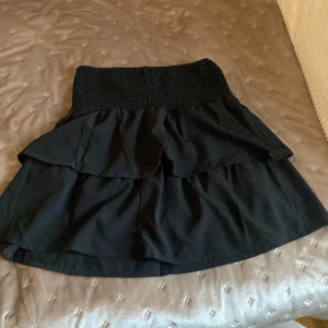 Svart kjol från Seaside - Snygg svart kjol från Seaside med volangdetaljer. Den har en elastisk midja som ger en bekväm passform. Perfekt för att skapa en stilren look. Även om det är en kjol så passar den bra och ha som tröja också. 