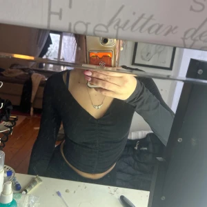 Svart långärmad topp från Iva Nikolina x NA-KD - Snygg svart långärmad topp från Iva Nikolina x NA-KD med v-ringning och rynkdetalj framtill. Perfekt för en stilren look. Säljes för använder inte💕